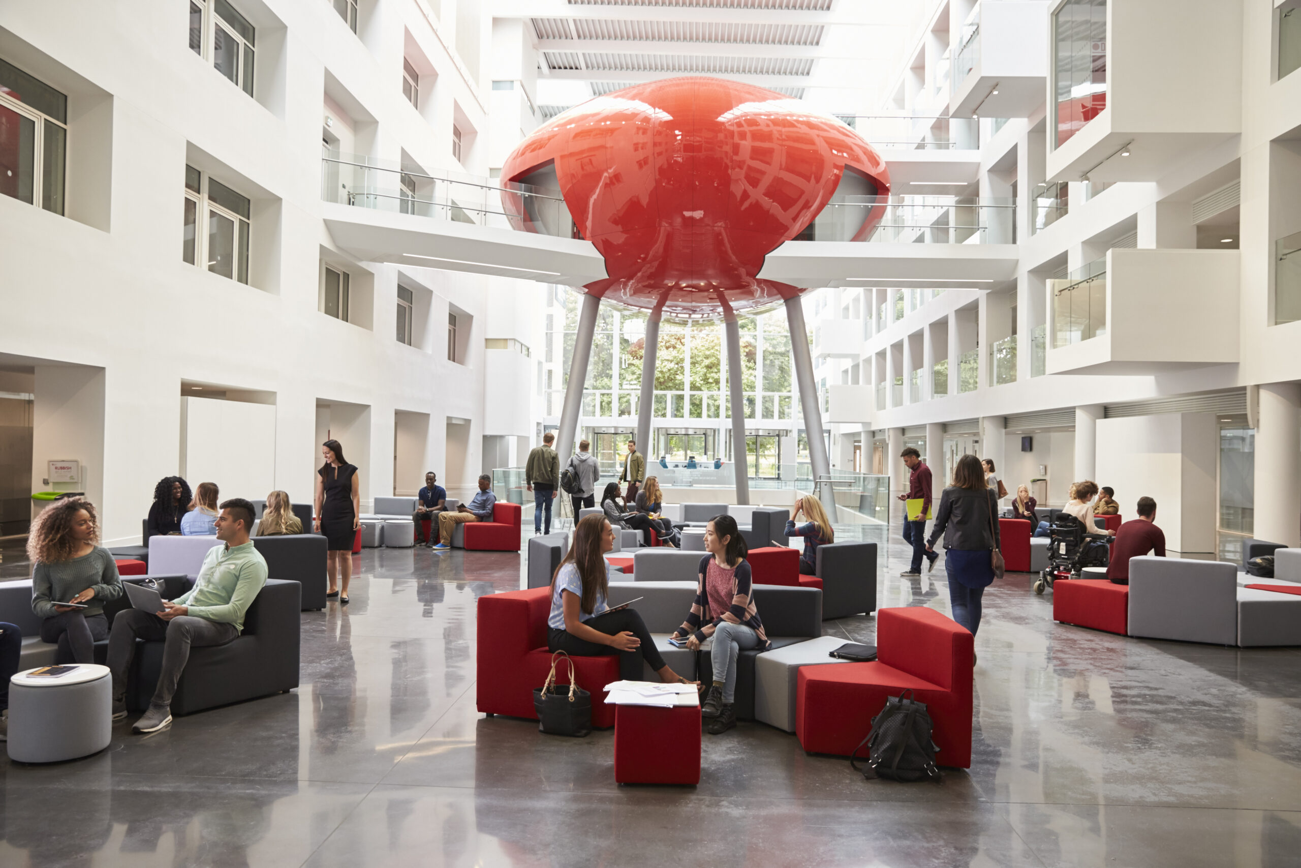 Students sit talking in the atrium lobby of their university